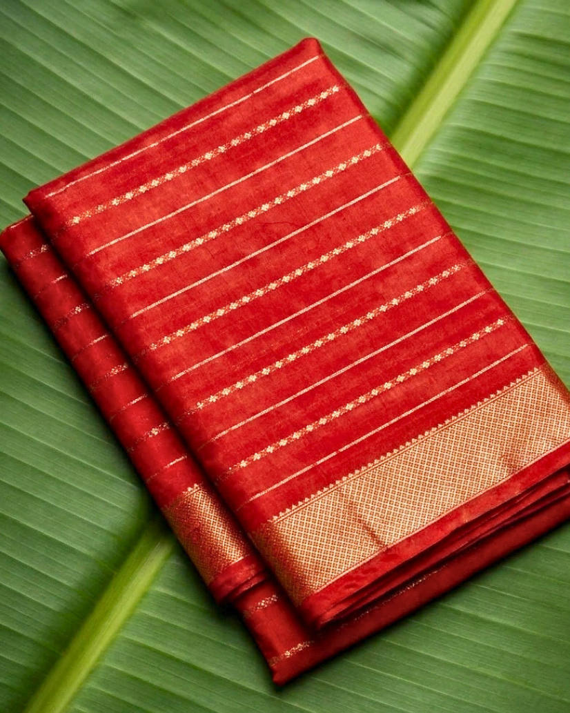A folded red saree with gold zari stripes and a beige border, displayed on a large green banana leaf. A beige banner at the bottom features the brand logo 'Nivih Wearz' and the text 'Maheswari - Red'.