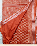 A folded and draped rust orange pure linen cotton sari with white floral and geometric block prints, displayed on a light background with a brand logo banner at the bottom.