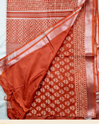 A folded and draped rust orange pure linen cotton sari with white floral and geometric block prints, displayed on a light background with a brand logo banner at the bottom.