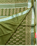 An olive green pure linen cotton saree with beige block prints and a silver border, shown folded on a light background with a brand logo banner at the bottom.